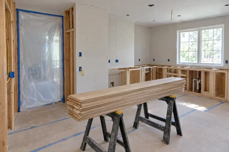 Kitchen under construction with open stud walls, plastic dust barriers and lumber on sawhorses